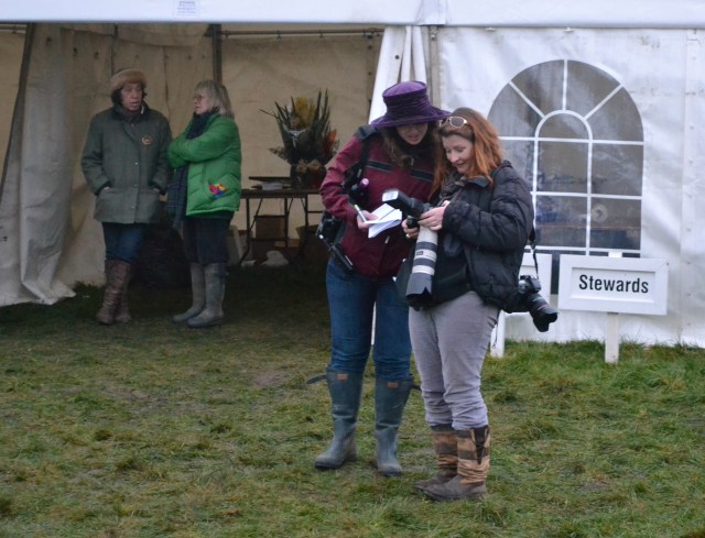 One race to go! Announcer Charlotte Russell (purple hat) checks out some of Louise Pollard's photos, in the background Honourable Secretary Christine Drury (fur headband) relaxes after a busy day